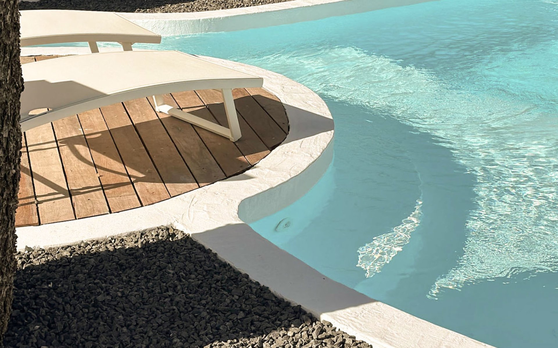 Pool edge with pale render, timber deck and gravel under bright daylight